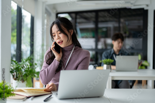 Free Download A beautiful Asian businesswoman makes a call to her client at her desk in the office. - GFXLoad