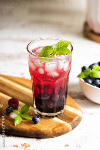 The glass of iced tea with berries on the wooden table.