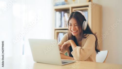 Young asian woman wearing headset while working on computer laptop at house. Work at home, Video conference, Video call, Student learning online class photo