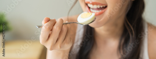 Protein in food  happy smiling asian young woman  girl in diet eat boiled egg  hand holding spoon put food in mouth with for breakfast in the morning at home. Health care  loss weight people concept.