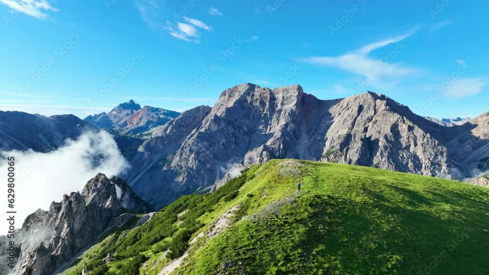 Revealing drone shot of a jagged, rugged mountain peak in Italy's Dolomite mountain range on a sunny summer day.