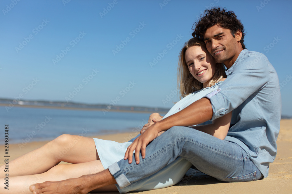 young couple sitting together on a sand by sea