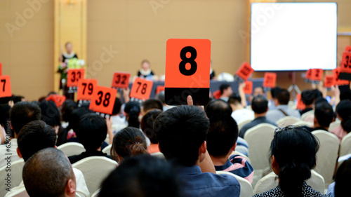Crowd of bidders holding their numbered bidding paddles at an auction