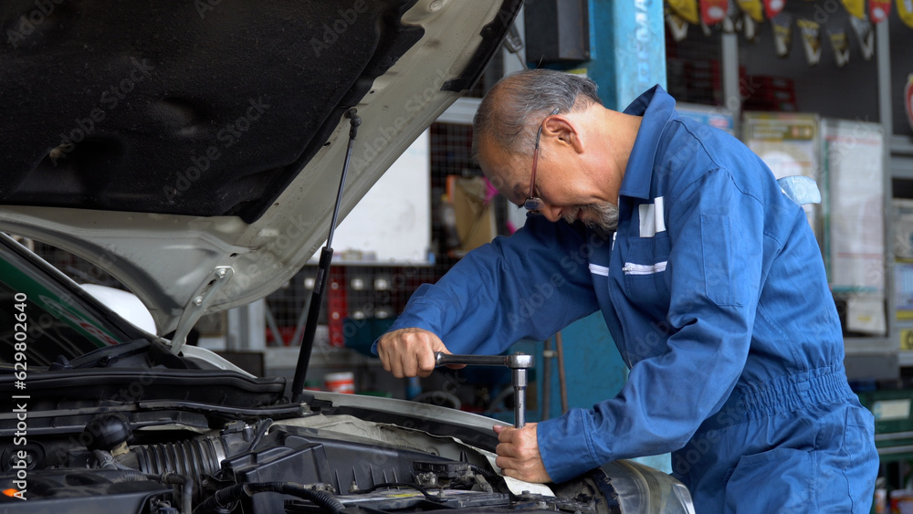 asian mechanic senior man using socket spanner wrench repairing a car in workshop at auto car repair service center. car engineer old man inspection vehicle details asian mechanic senior man using socket spanner wrench repairing a car in workshop at auto car repair service center. car engineer old man inspection vehicle details