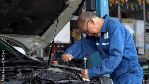 asian mechanic senior man using socket spanner wrench repairing a car in workshop at auto car repair service center. car engineer old man inspection vehicle details