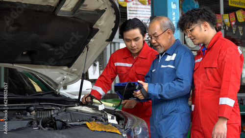 senior asian car mechanic manager training apprentice to checking car engine by Diagnostics Software repair in garage . old asia Auto mechanic teaching trainee or assistant on the repair shop . © iammotos