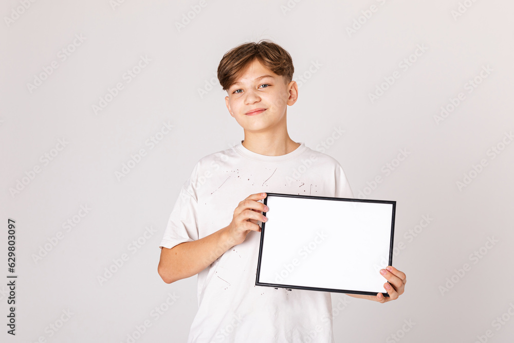 Attractive teenage boy holding a blank sign on white background. Banner. Young smiling boy show blank board. Close up male model portrait on white background. Attractive teenage boy holding a blank sign on white background. Banner. Young smiling boy show blank board. Close up male model portrait on white background.