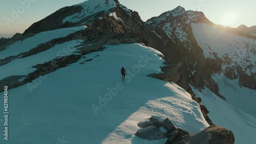 Drone shot from behind of a female mountaineer hiking across a scenic snowfield at sunrise in the mountains of South Tyrol, Italy.