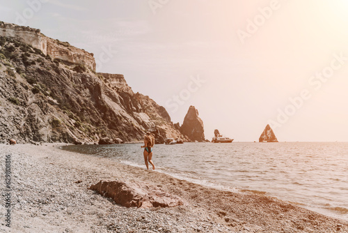 Woman travel summer sea. A happy tourist in a blue bikini enjoying the scenic view of the sea and volcanic mountains while taking pictures to capture the memories of her travel adventure.