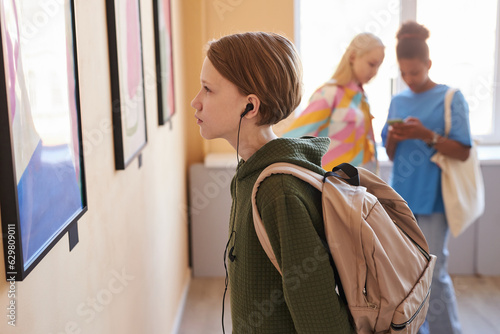 Side view portrait of young teenage boy looking at picture in art gallery or museum, copy space photo