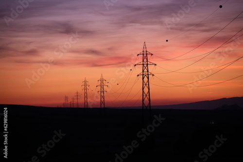 Silhouettes of high voltage lines running across vast land at red sunset