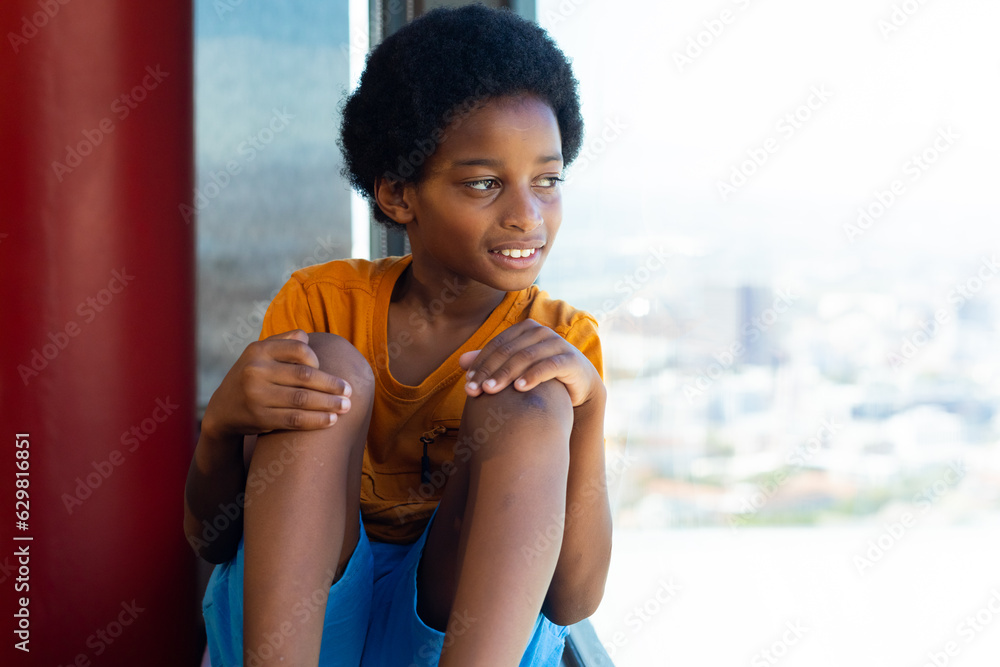 Happy biracial schoolboy wearing yellow tshirt and looking through window in classroom Happy biracial schoolboy wearing yellow tshirt and looking through window in classroom