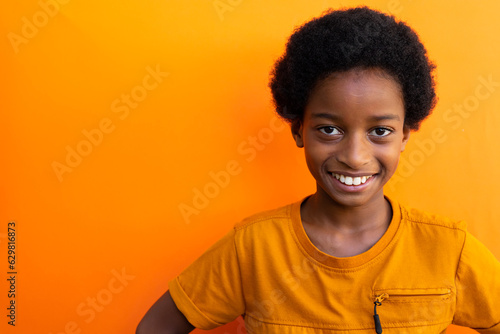 Portrait of happy biracial schoolboy wearing yellow tshirt over orange background, copy space