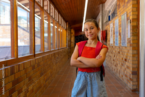Portrait of happy caucasian schoolgirl with school bag in corridor at elementary school, copy space
