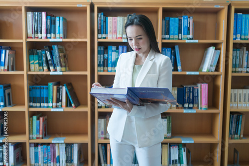 A female university lecturer in a business suit is searching for the book on the bookshelf in the library