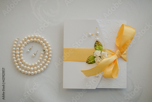 Costume jewelry for the bride: earrings and beads made of artificial pearls. Wedding invitation with yellow satin ribbon and flowers
