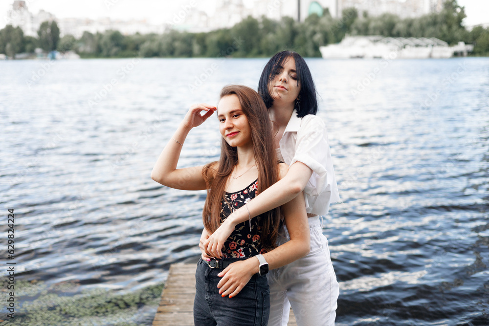 Two teenager girls sitting on a pier at the river bank having good time in summer. happy girl friends relaxing outdoor near lake.
