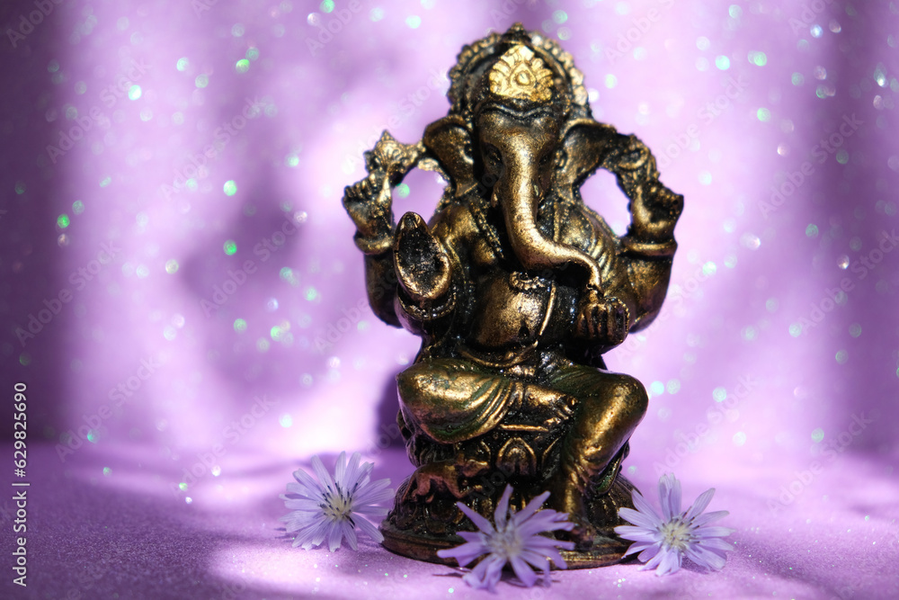 Deity of Ganesha on beautiful purple pink background, flowers and glare lights