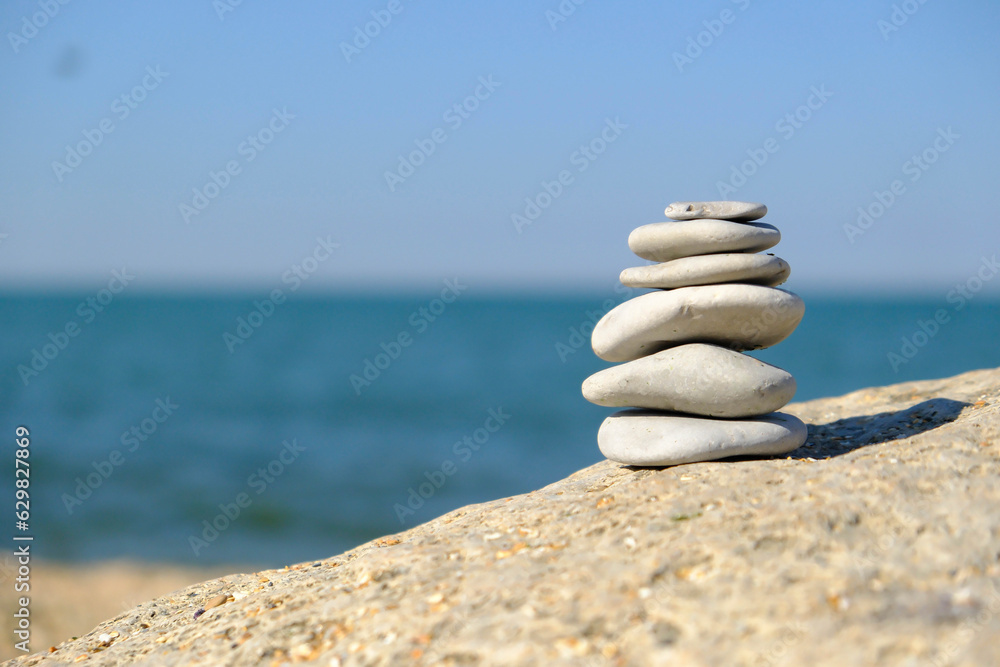 Fototapeta premium Pebble tower balance harmony stones arrangment on sea beach coastline. Spa therapy summer travel vacation.