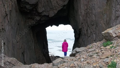 Blonde in pink jacket by hole through Torghatten mountain; drone crane reveal photo