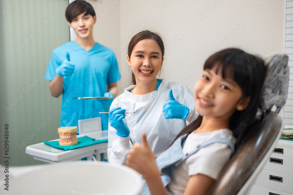 Fototapeta premium Children's dentistry for healthy teeth .Close-up happy little child asian girl smiles looking at camera, sitting in dentist's chair, receiving dental.
