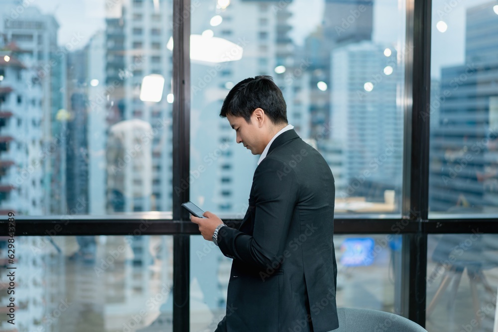 Handsome young man sitting by the window in the office using a smartphone communication concept The background is a city view.