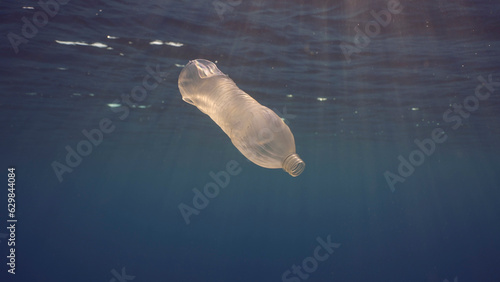 Disposable plastic bottle drift under surface of water in bright sunrays. A plastic bottle is thrown into the sea slowly drifts in water column in rays of morning sun, Red sea, Egypt