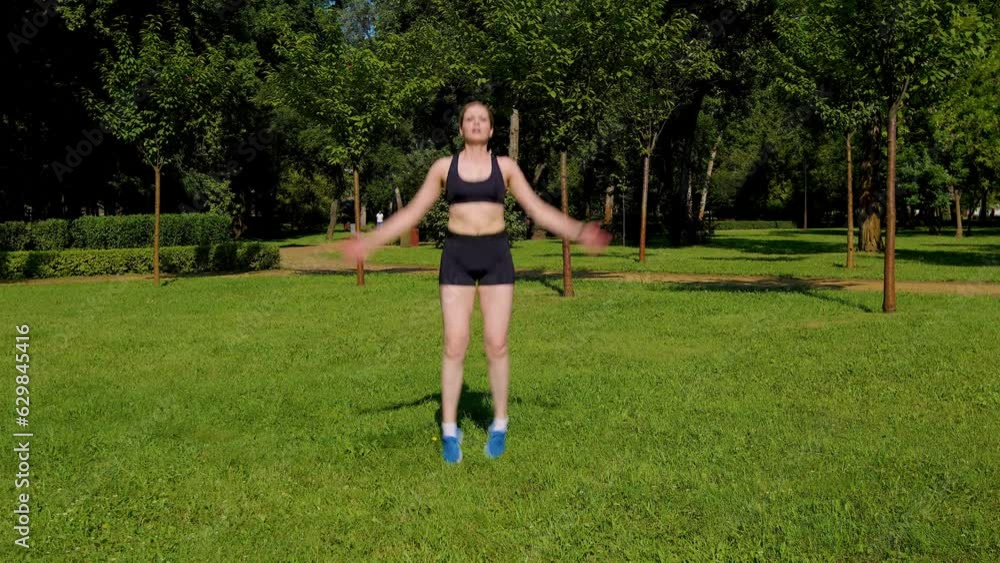 Motivated sporty fit attractive middle aged woman in activewear doing jumping jack exercise on park green lawn, improving cardiovascular fitness. and mobility, increasing hip and leg strength. Motivated sporty fit attractive middle aged woman in activewear doing jumping jack exercise on park green lawn, improving cardiovascular fitness. and mobility, increasing hip and leg strength.