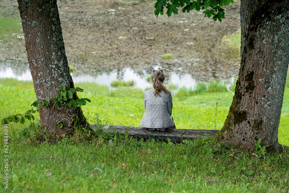 A woman sits among the trees on the banks of the river. Relax. The concept of loneliness. Selective focus. A woman sits among the trees on the banks of the river. Relax. The concept of loneliness. Selective focus.
