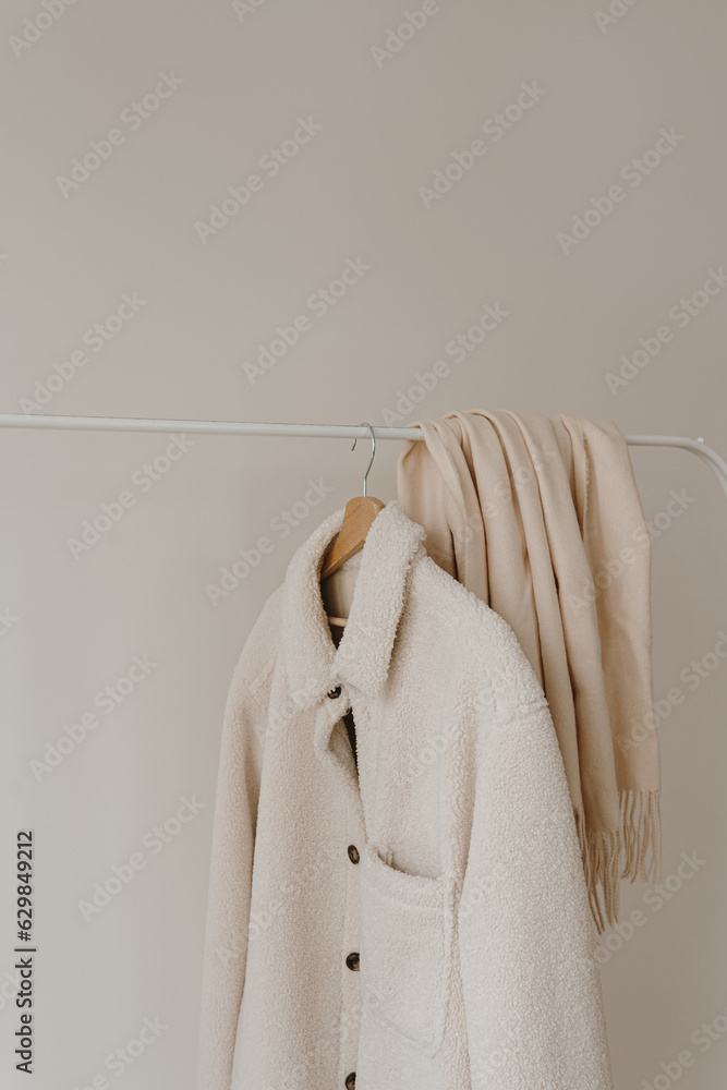 White warm woolen autumn seasonal jacket and skirt on hanger over white wall. Minimalist fashion clothes wardrobe White warm woolen autumn seasonal jacket and skirt on hanger over white wall. Minimalist fashion clothes wardrobe