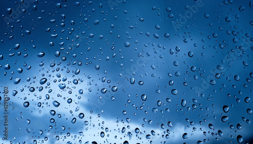 Water drops on a glass pane in front of dark rain clouds in blue color