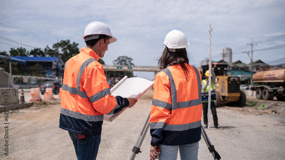 Portrait surveyors wearing uniform conversation and blueprint check inspection by theodolite camera to measurement level position road construction site is industry transportation concept Portrait surveyors wearing uniform conversation and blueprint check inspection by theodolite camera to measurement level position road construction site is industry transportation concept