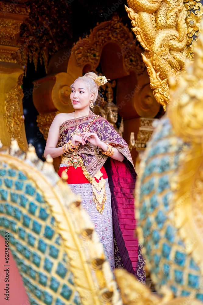 Vertical image of Asian woman wear Thai traditional dress stand in front of temple door and look to left side with happiness and she look like tourist who travel in landmark of Thailand.