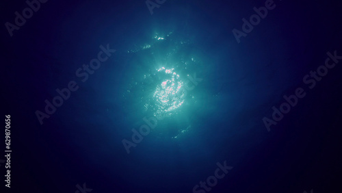 View of sun light from blue abyss, slow motion. Light filters down through blue water. Underwater sun rays in depth ocean. Underwater light, sun light shine under deep water with ripples on surface