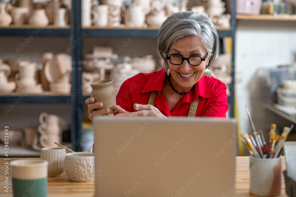 Senior woman potter broadcasting live lesson masterclass painting clay products, teaching students online. Senior woman potter broadcasting live lesson masterclass painting clay products, teaching students online.