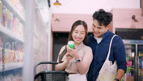 Millennial Asian couple family shopping groceries in supermarket buying food checking item label in convenience store indoors. Asia customers purchasing food supply while standing in front of shelves
