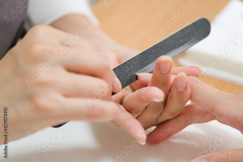 ネイリストにネイルファイルで爪を整えてもらっている女性の指先のクローズアップ