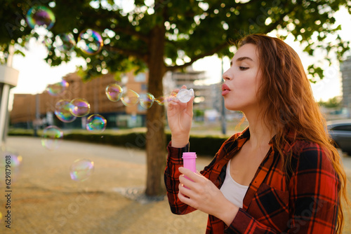 Young woman has fun blowing soap bubbles standing on the street. 