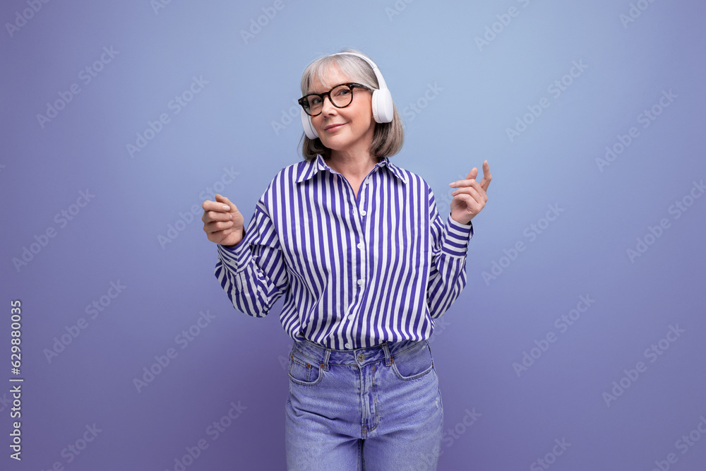 Fototapeta premium Energetic retired woman with gray hair masters headphone technique on a bright studio background
