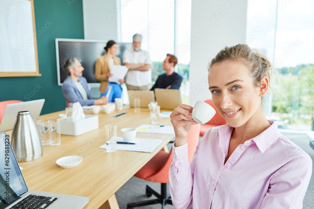 Obraz premium Portrait of smiling businesswoman drinking coffee sitting near team discussing in conference room at office