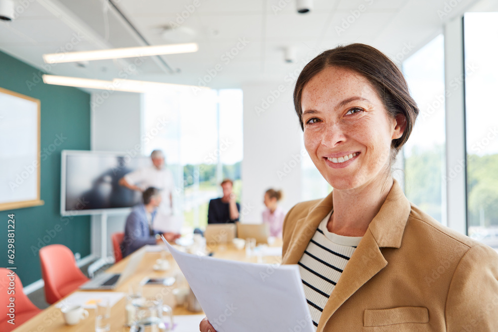 Fototapeta premium Portrait of smiling businesswoman with document against colleagues in conference room at office