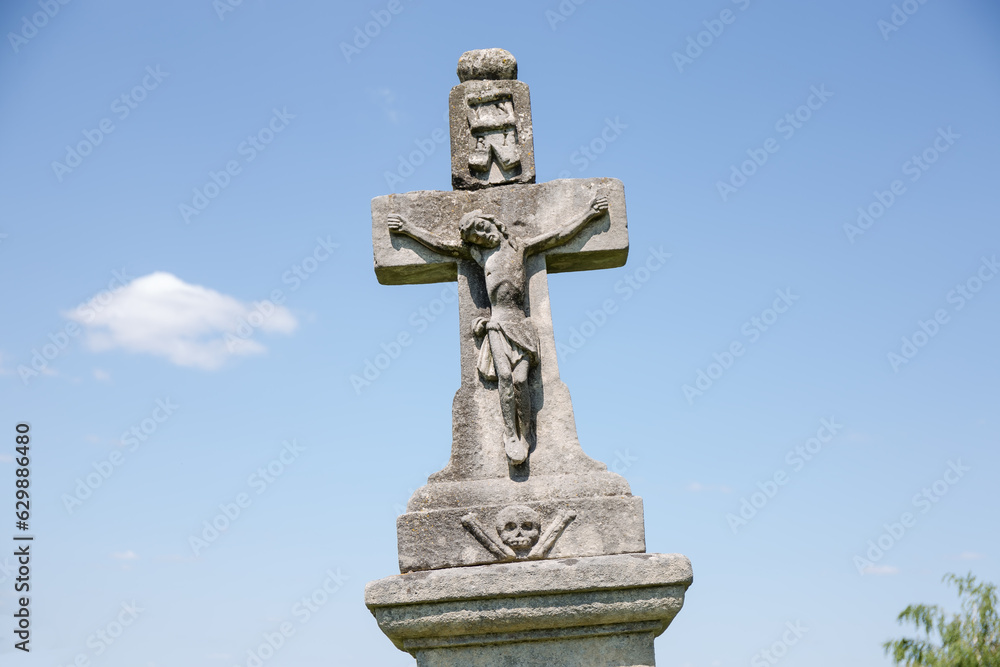 Ancient stone tombstone in form of crucified Jesus on cemetery