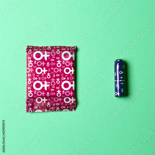 A sanitary napkin and a tampon lie on a green background. View from above. Gasket in red packaging. A tampon in a lilac package. Square image. Flatley