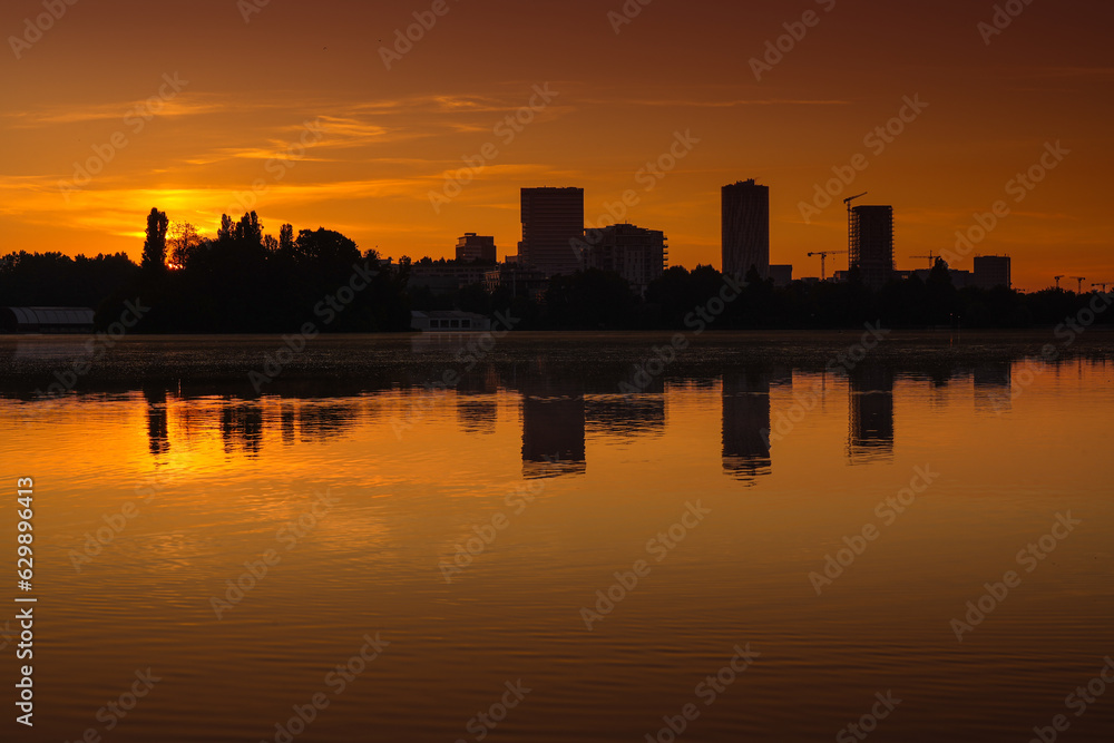 Bucharest at sunrise. beautiful morning orange sky landscape of the city skyline and its reflection in Herastrau Lake. Travel to Romania.