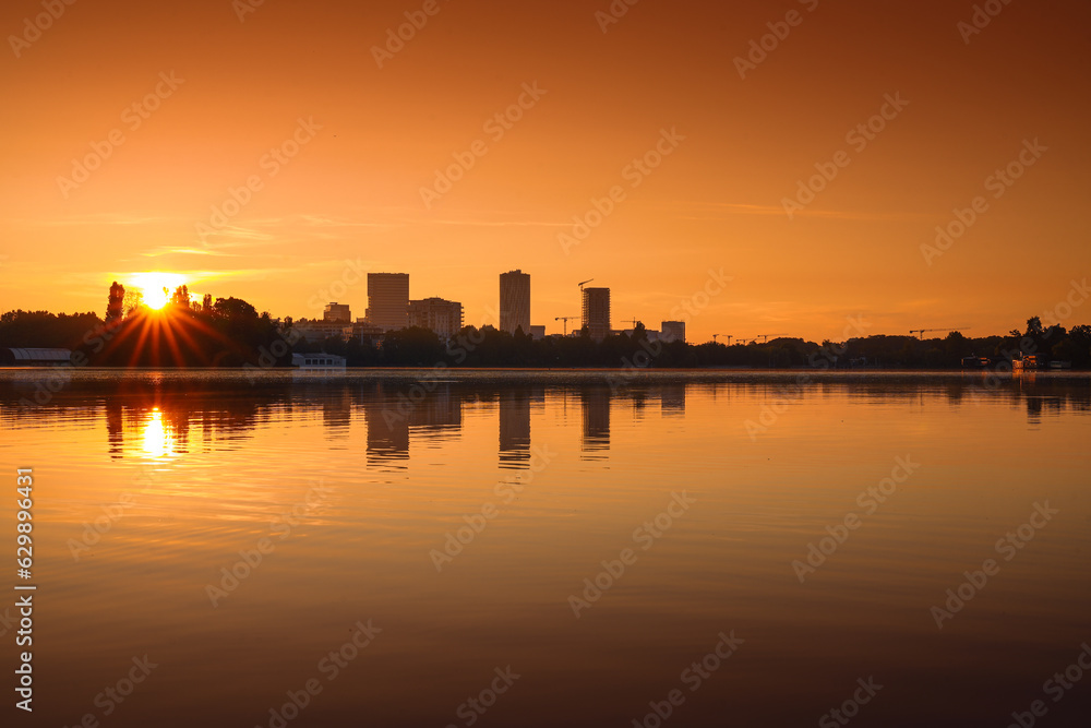 Bucharest at sunrise. beautiful morning orange sky landscape of the city skyline and its reflection in Herastrau Lake. Travel to Romania.