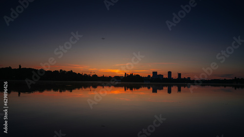 Sunrise over Bucharest. Sunrise photo in the morning dusk with orange and blue sky with the skyline of Bucharest and reflection in Herastrau Lake. Travel to Romania.