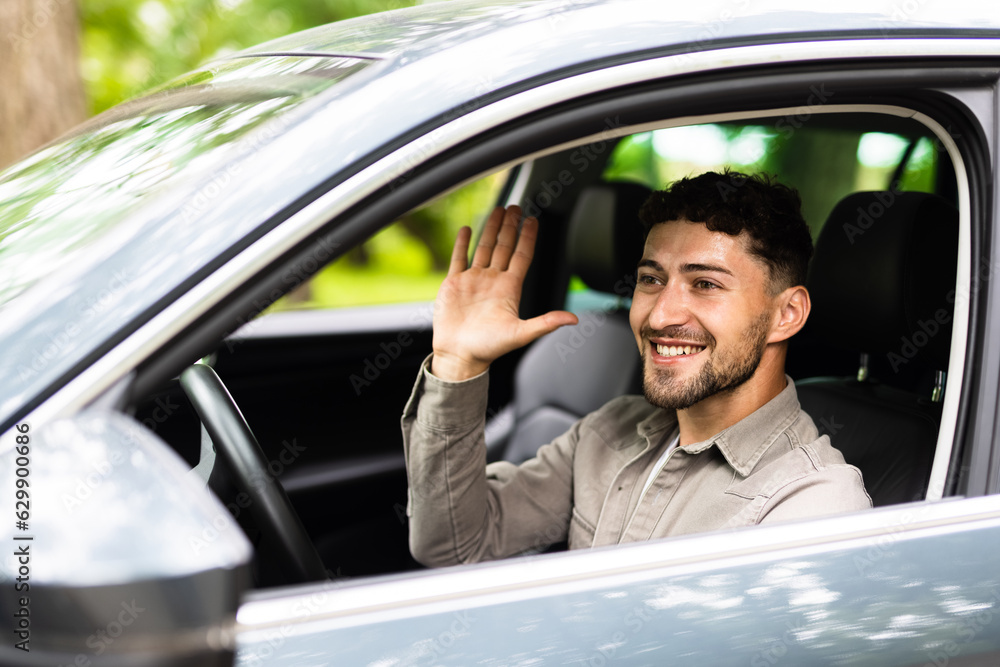 Young man waves his hand in greeting while driving