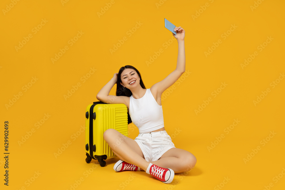 An Asian girl sits near a suitcase, on a yellow background