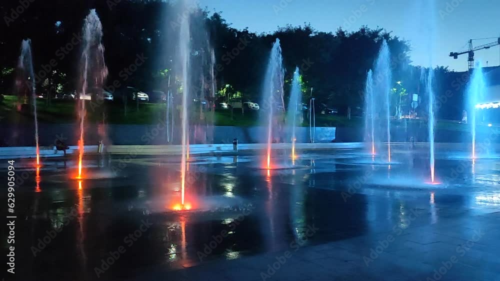 Pedestrian ground fountain illuminated by colorful lights at night. Big public street fountains illuminated by multi-colored light in city. Jets of water rise up and fall splashes down. Water Splash Pedestrian ground fountain illuminated by colorful lights at night. Big public street fountains illuminated by multi-colored light in city. Jets of water rise up and fall splashes down. Water Splash