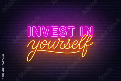 Invest in yourself neon lettering on brick wall background.